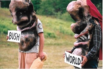 Two people wearing costumes and holding signs that say "Bush" and "World".