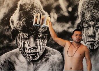 A shirtless man holds up a book.