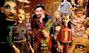 A puppeteer stands surrounded by large marionette puppets.
