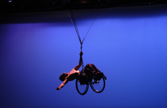 A performer in a wheelchair suspended in midair by a wire.