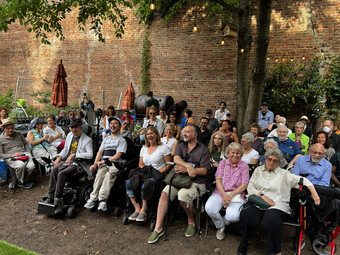 A large group of people are seated in front of a brick wall, facing the camera.