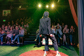 A performer standing under spotlights on a stage in front of an audience.