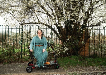 A woman sitting outside on a scooter in front of a flowering tree.