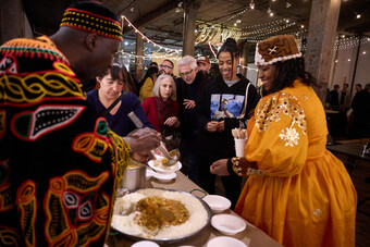 A group of people surrounds a table serving food in a festive setting.