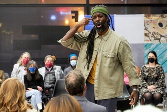 A tall Black man performs passionately while surrounded by audience members.