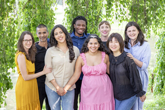 The eight members of the HowlRound team smile for a group photo in front of a tree.