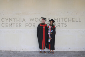 Two people pose in graduation attire.