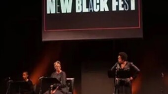 Three people on stage in front of a projection screen that reads, "New Black Fest."