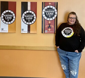 A woman stands in front of a series of posters reading You Are On Native Land.