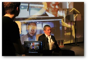 An actor performs in front of a live projection of themselves as they are being recorded.