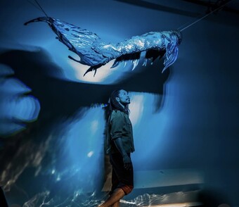 A person in blue lighting looks up at a sculpture. 