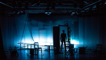 A stage with chairs turned over and a person standing in an open doorway. 