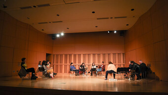 artists sitting in a circle on chairs on a stage.