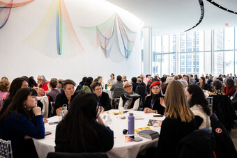 A crowded room with people sitting at round tables. 