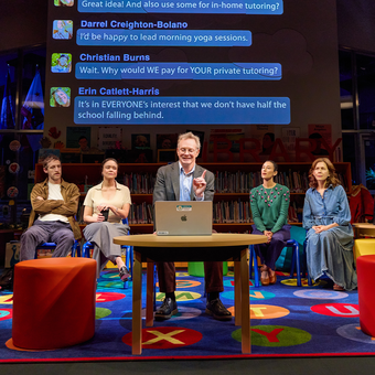 A person sitting behind a laptop and four people sitting in a row behind them in a classroom like stage set. 