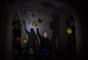 Three people in dark clothes in a dimly lit room throwing yellow construction hats in the hair.