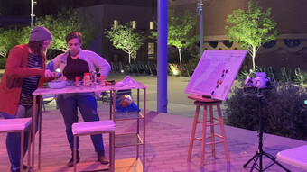 Two people and an easel outside in neon purple light.