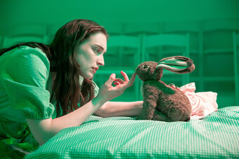 A woman pointing at a stuffed bunny in green light.