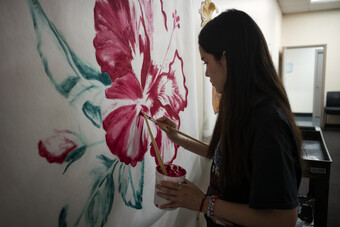 A woman painting a pink hibiscus flower on a wall.
