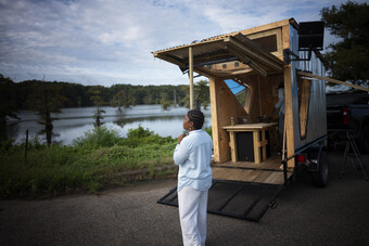 A person in all white standing near a tiny home.