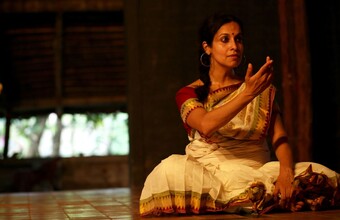 A woman in traditional Indian attire sitting on the floor holding her hand in front of her.