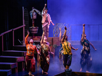 A group of actors in colorful clothes dancing on a stairway set.