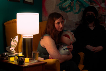 A person sitting in a dimly lit room holding a puppet of an old man.
