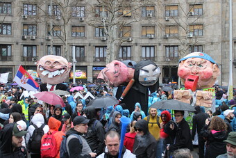 A group of people outside at a festival with large puppets.