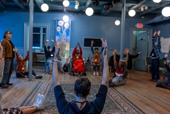 A group of people sit on the floor and stretch their arms up