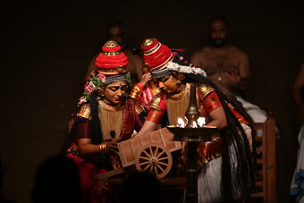 Two people dressed in traditional Indian clothing looking at a little brown cart.