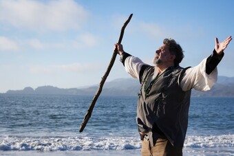 A man stands with his arms outstretched before a body of water.