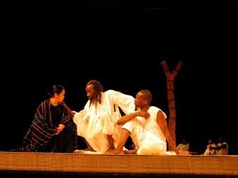Three people kneel together onstage.