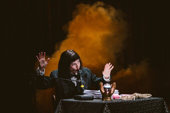 A woman with black hair sits at a desk onstage.