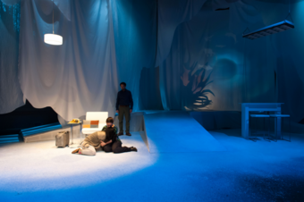 Actors embrace on a white stage.