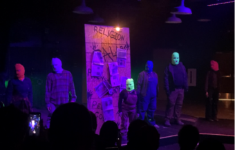 A group of people in balaclavas perform onstage.