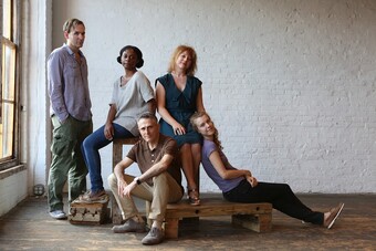 Five actors pose for a group photo in front of a white wall with a window on the left.
