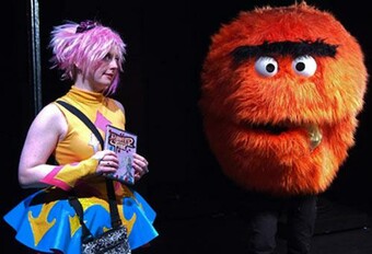 A performer wearing cosplay stands next to another performer in a large puppet costume.