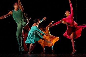 Five dancers in motion wearing monochromatic costumes