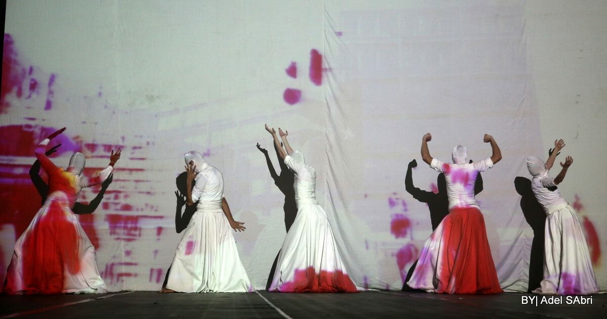 five performers in white dance against a wall with projection