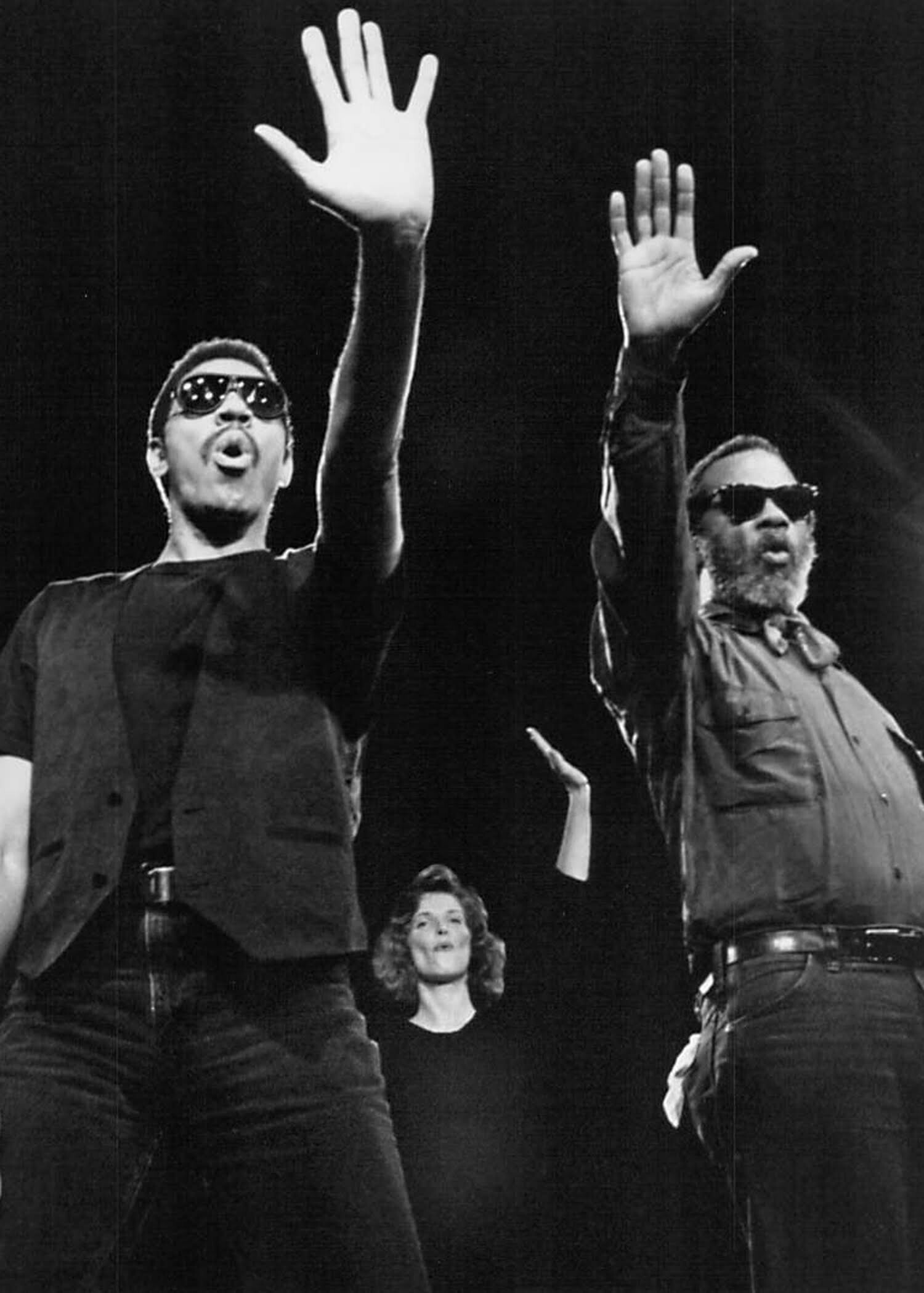 three performers wearing sunglasses with outstretched hands