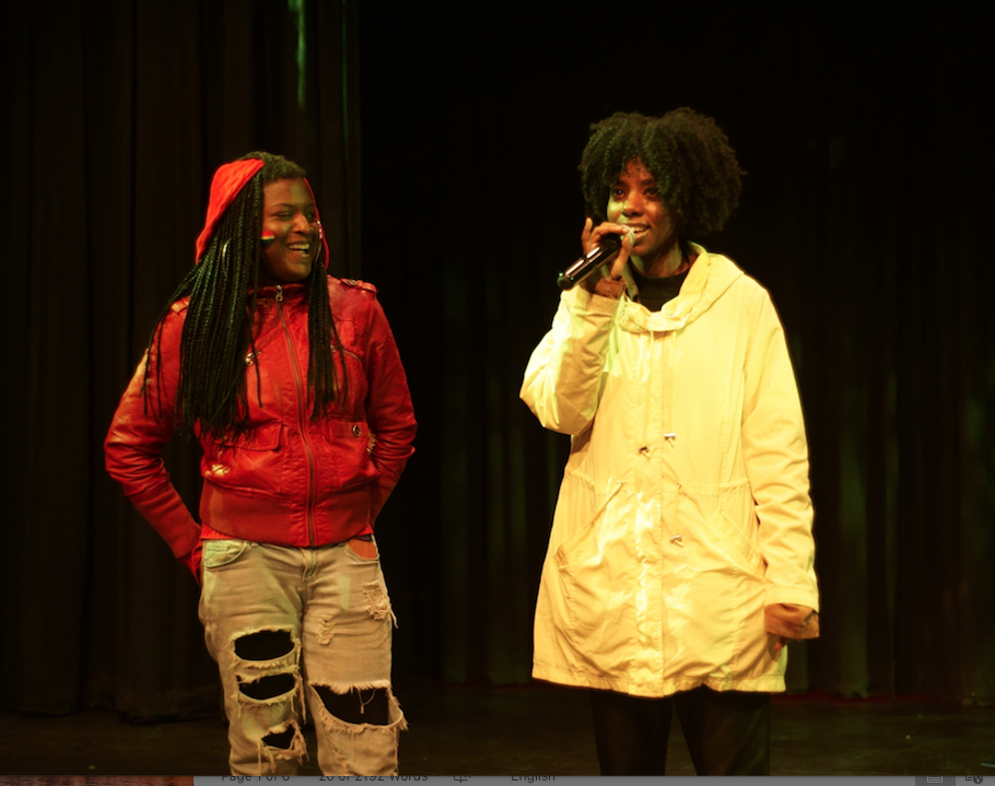 two performers smiling onstage, one holding a mic