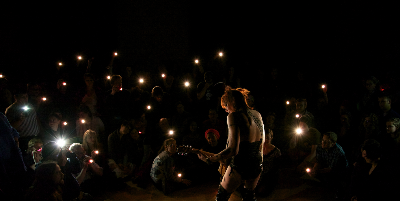 silhouette of performer playing guitar to a crowd of people holding flashlights