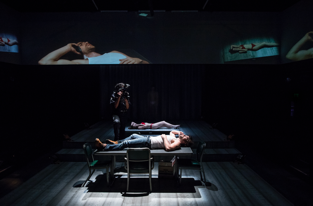 person lying down onstage, surrounded by screens.