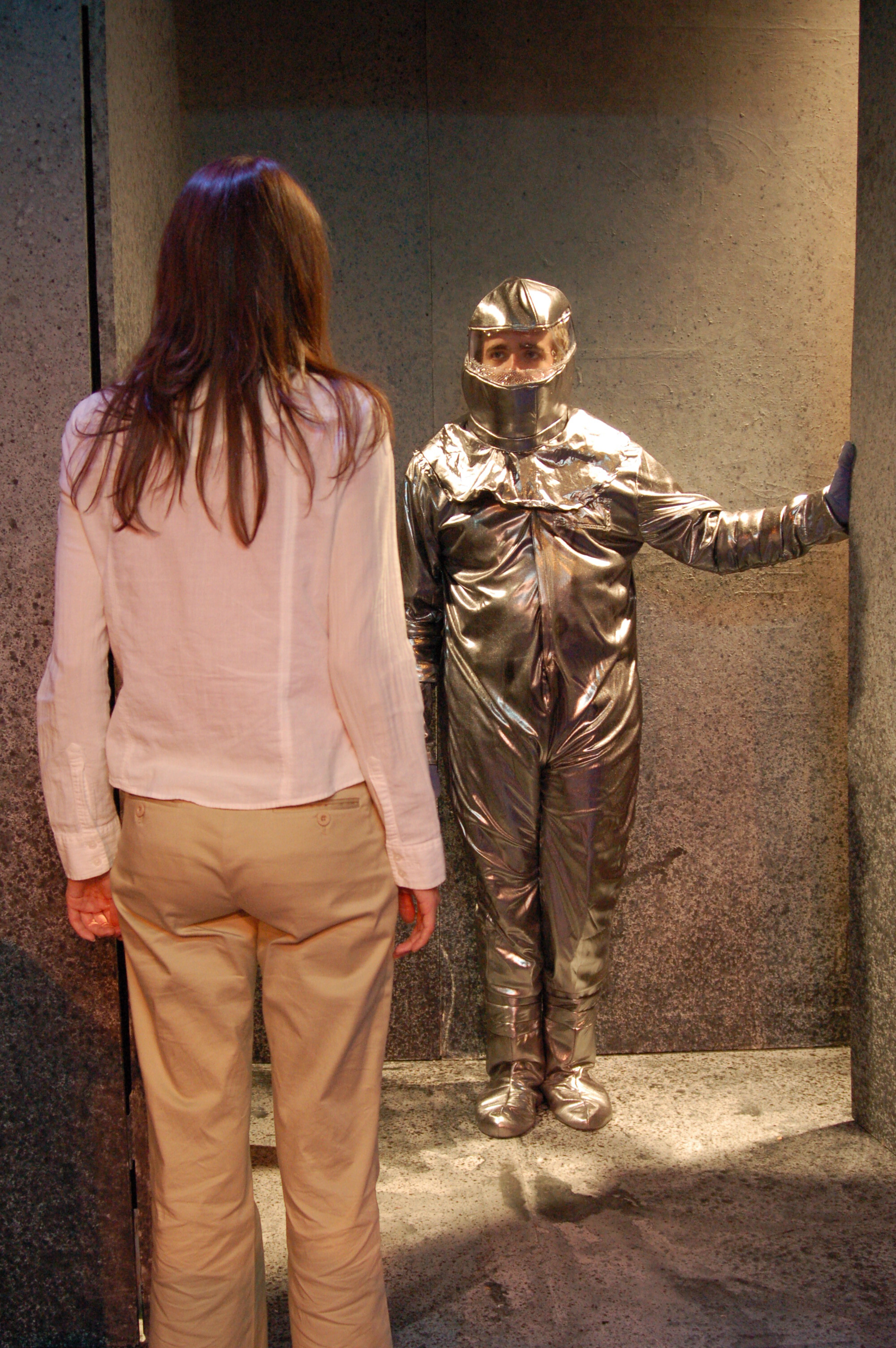 two actors stand towards each other, one in a silver suit
