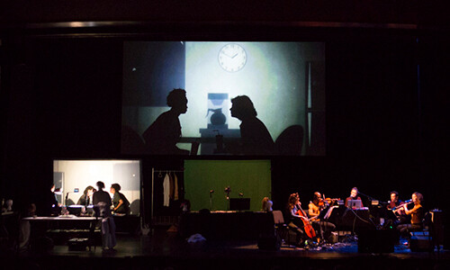actors and musicians onstage underneath a projection