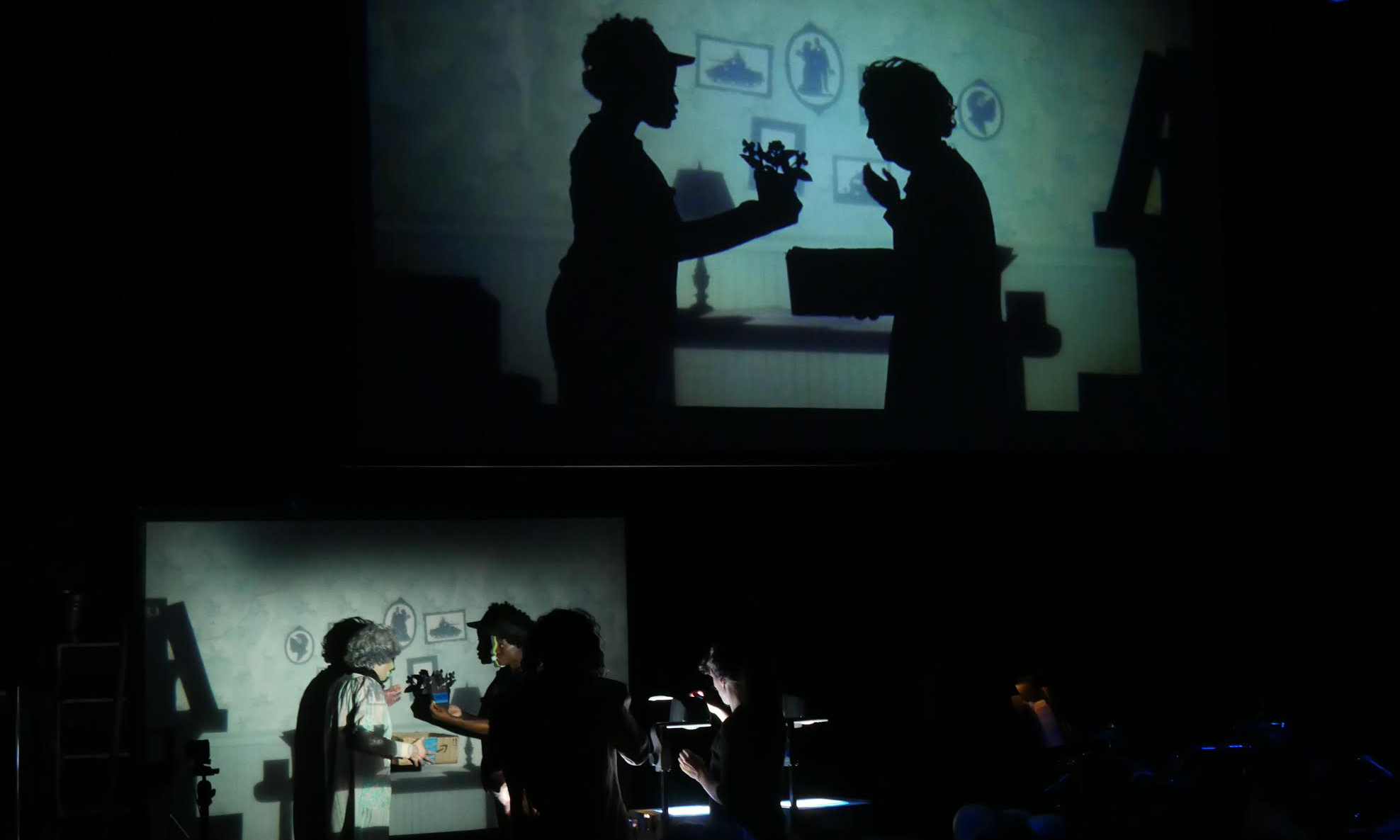actors onstage with a large shadowed projection above