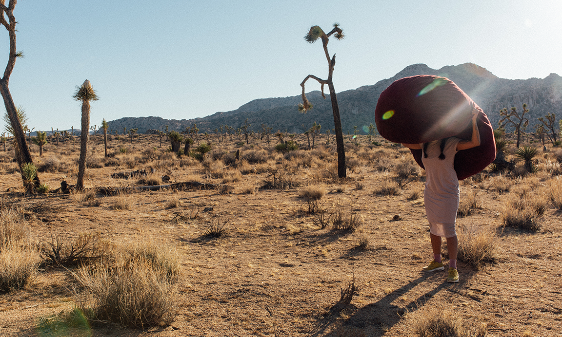 a person with a large bean bag over their head standing alone in the desert