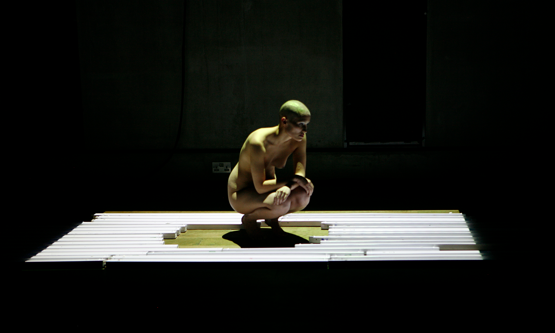 a nude person crouching on a brightly lit platform