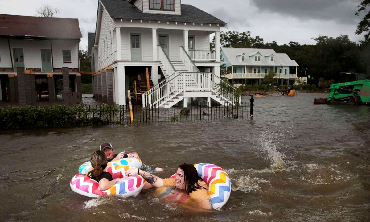 three people in tubes floating in flood waters outside their homes