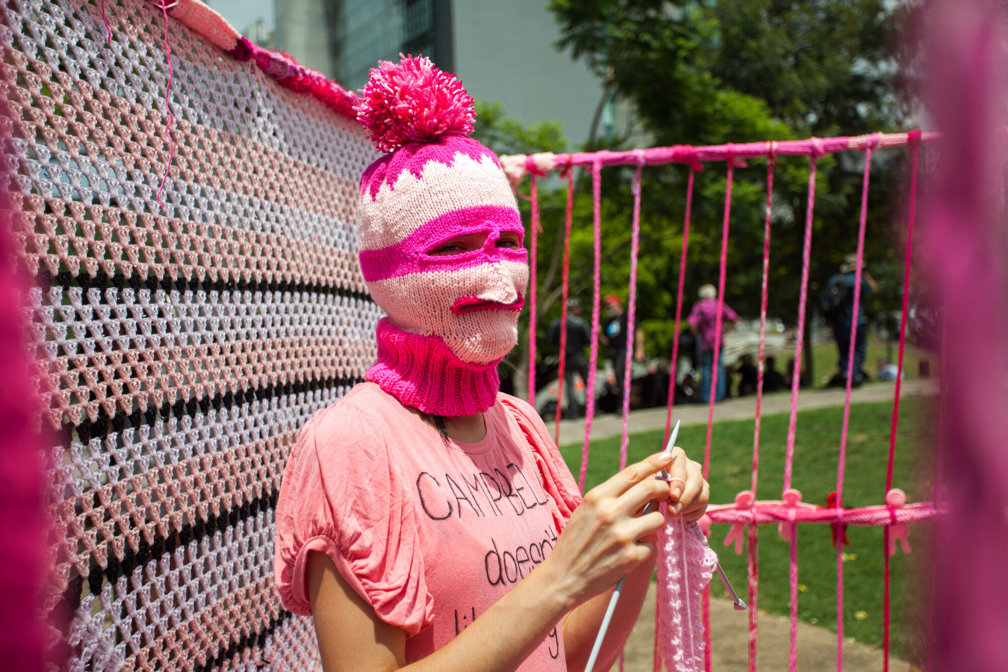 performer with pink hat covering their face, knitting, and surrounded by yarn.